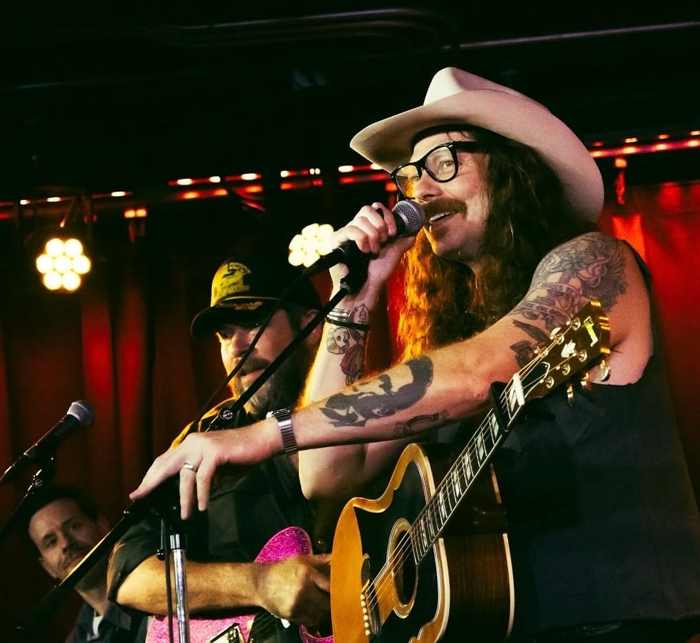 A country singer with a guitar on stage with two other musicians