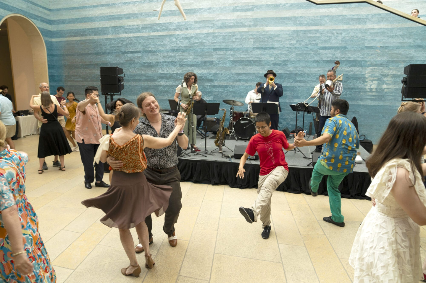 Group of people swing dancing in front of a band performing in the atrium of the Blanton Museum of Art, with the art installation 