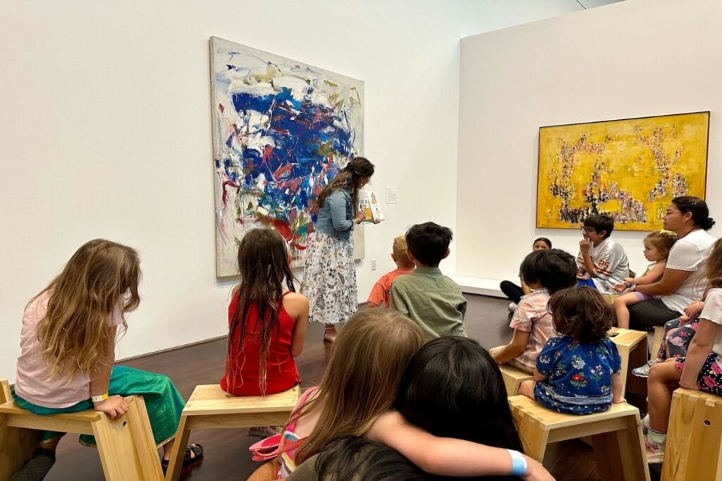 A group of family and kids listening to a story inside the Blanton Museum of Art, surrounded by art on the walls